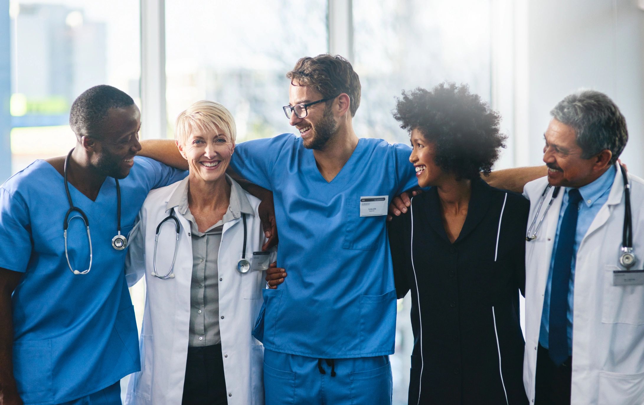 A diverse group of medical professionals smiling and embracing each other.